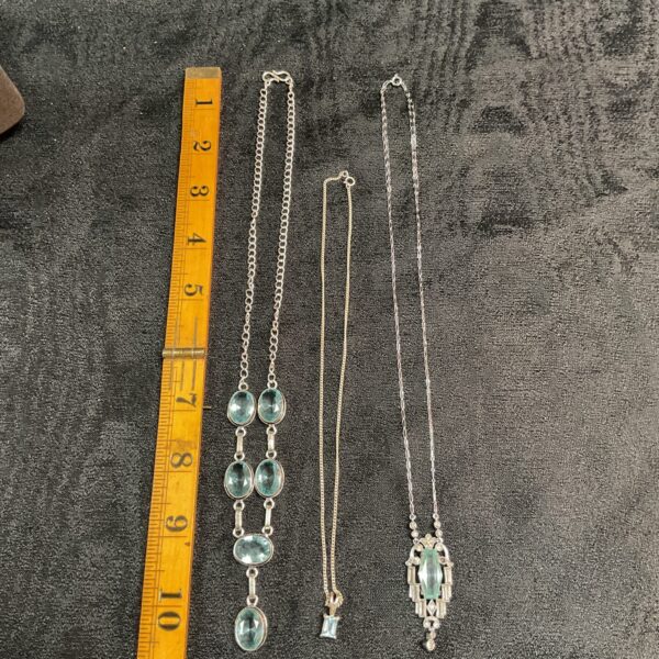 Collection of three silver necklaces with blue topaz pendants.