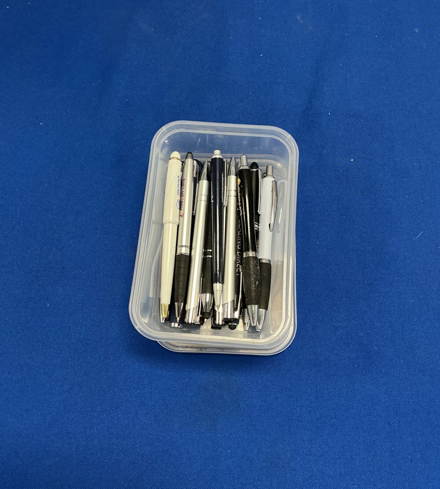 Clear plastic box filled with assorted pens and writing instruments.