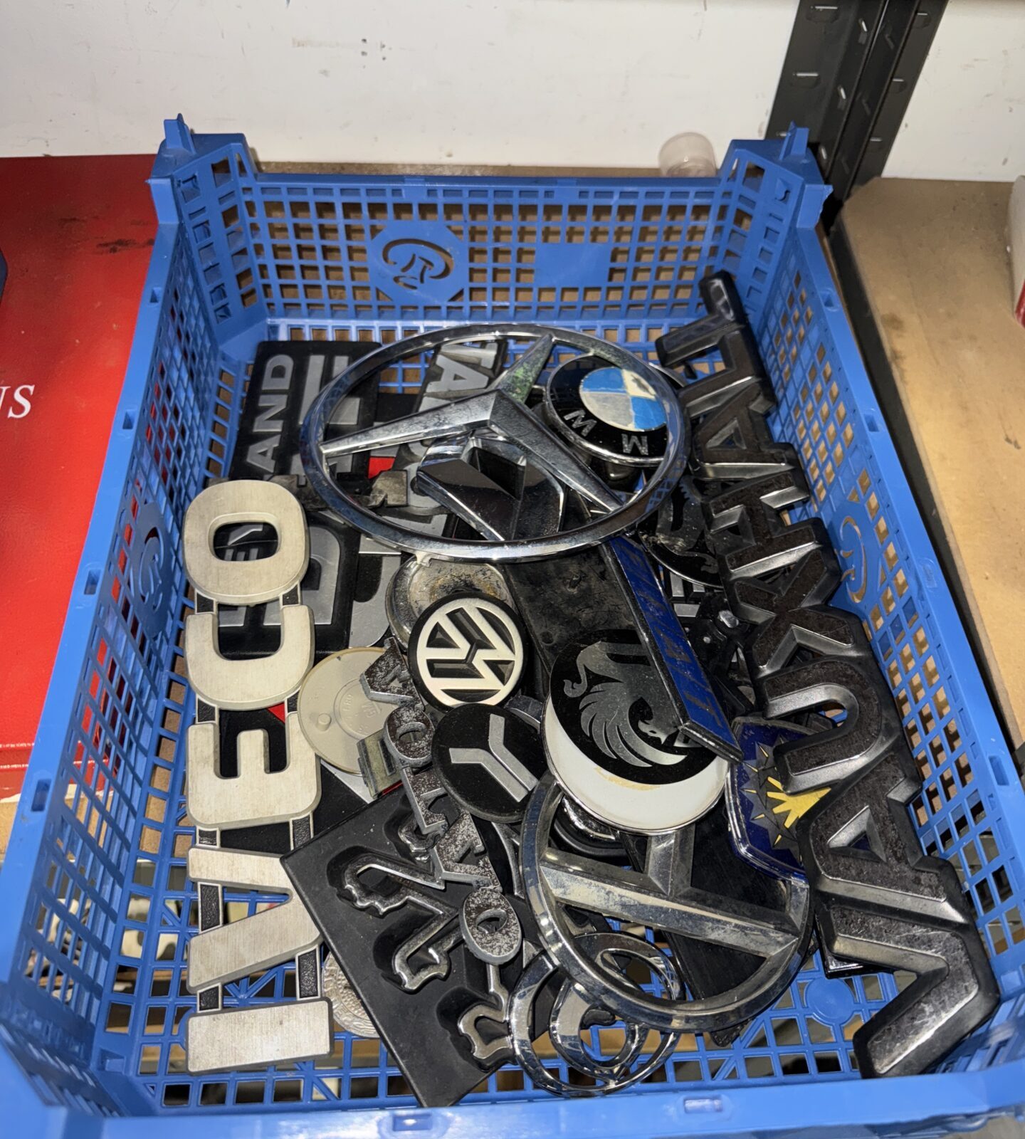 Assorted car and van badges in a plastic crate.