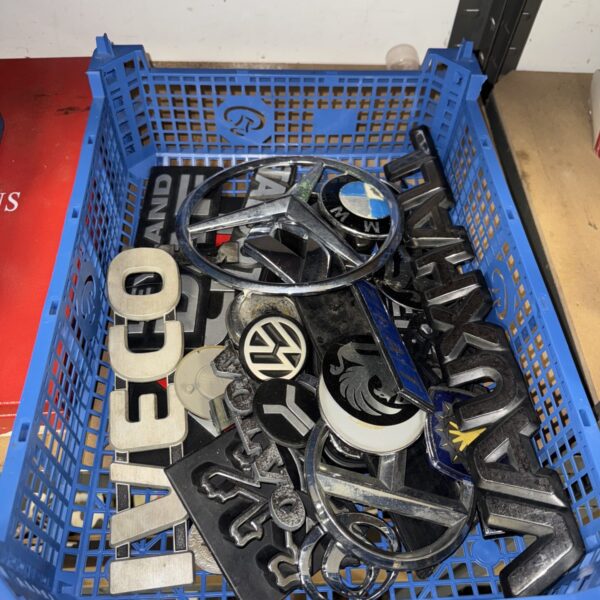 Assorted car and van badges in a plastic crate.