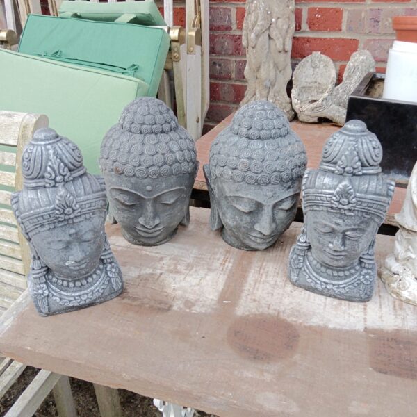 Four weathered cast stone Buddha heads displayed outdoors.