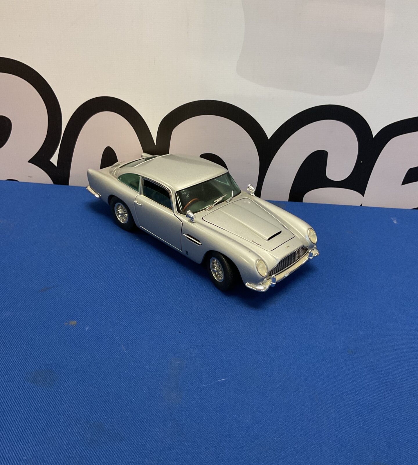 Silver Chrono Aston Martin DB5 model car on blue surface.