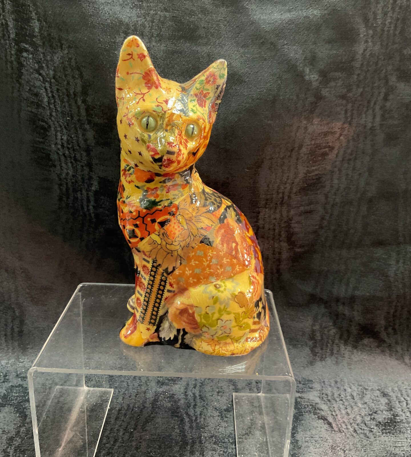 Colourful decoupage cat figurine on a clear stand.