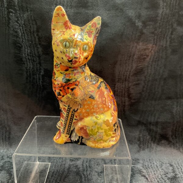 Colourful decoupage cat figurine on a clear stand.