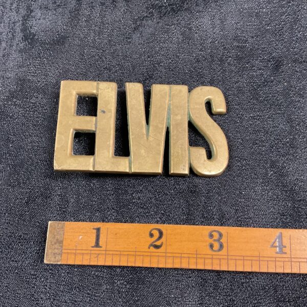 Vintage brass Elvis Baron buckle on dark background.