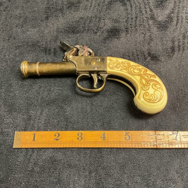 Brass flintlock derringer replica, antique style collectible firearm.