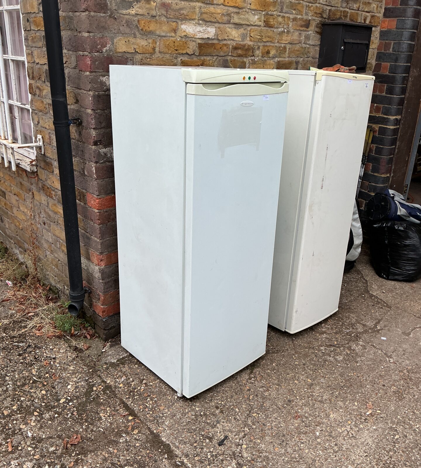 White Frigidaire tall freezer standing outside a building.