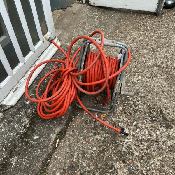 Red reinforced garden hose neatly wound on a metal reel.