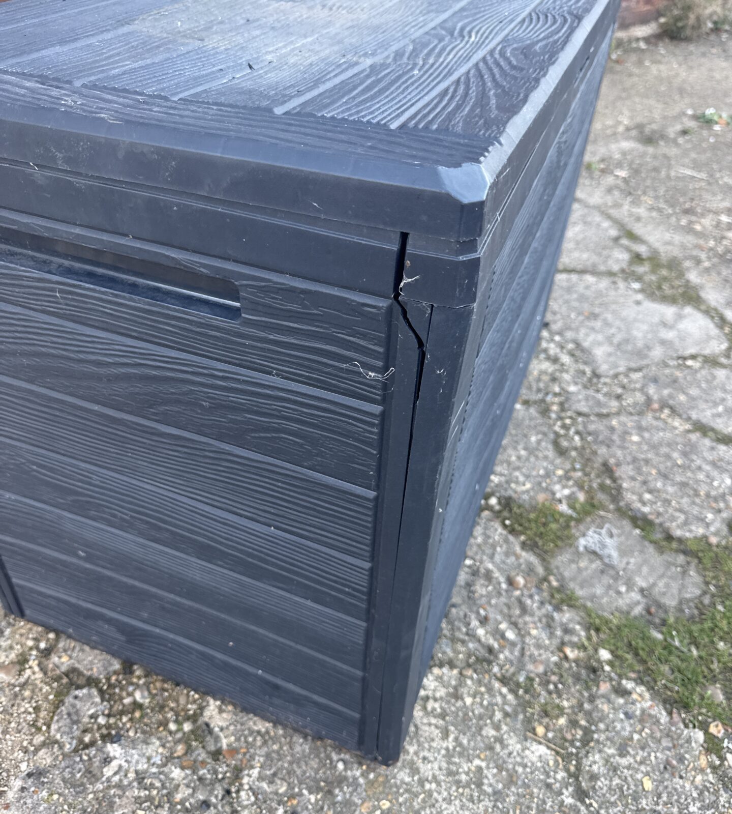 Close-up of damage to the side of a black garden storage bin.