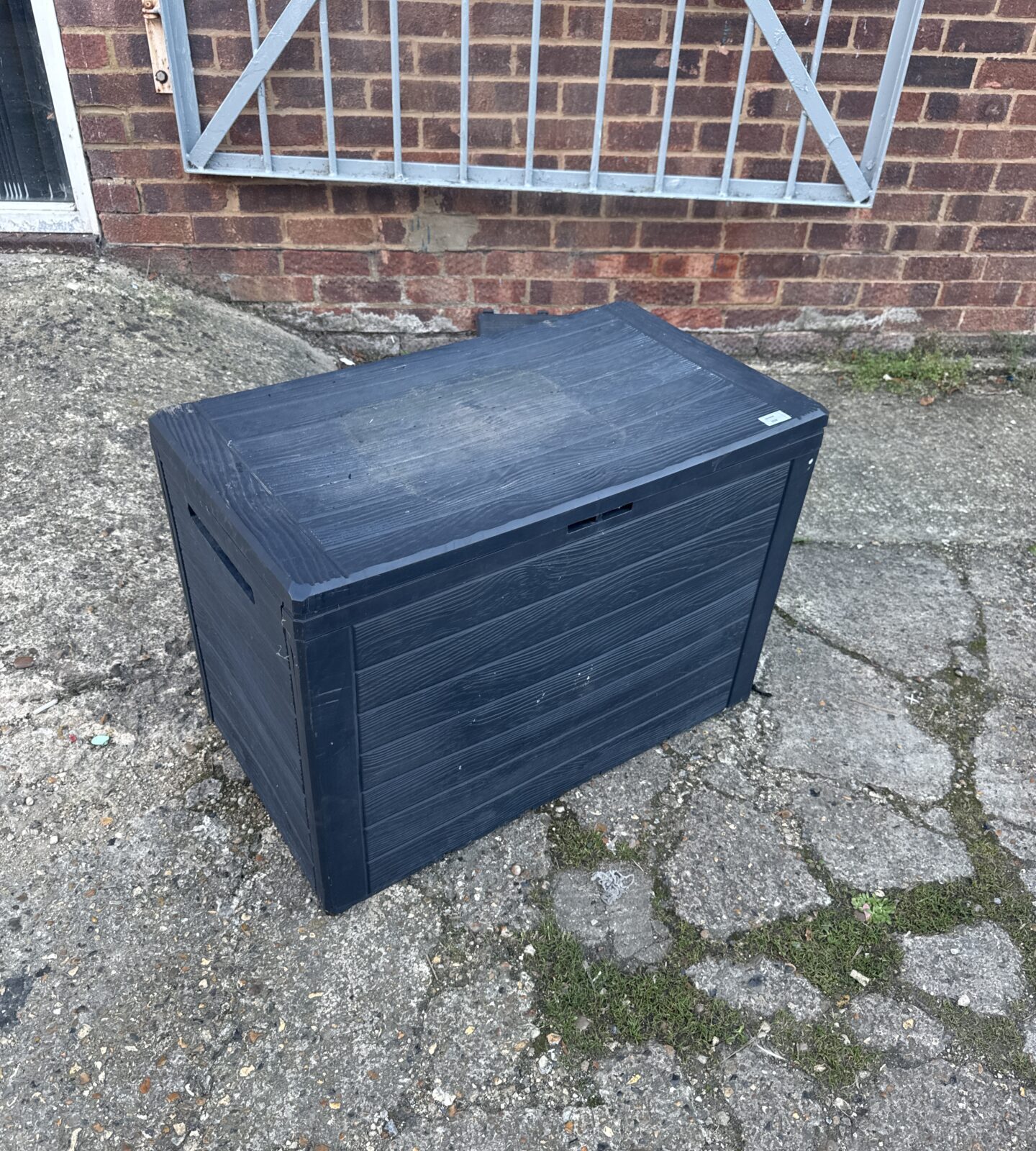 Black plastic garden storage bin in a garden setting.