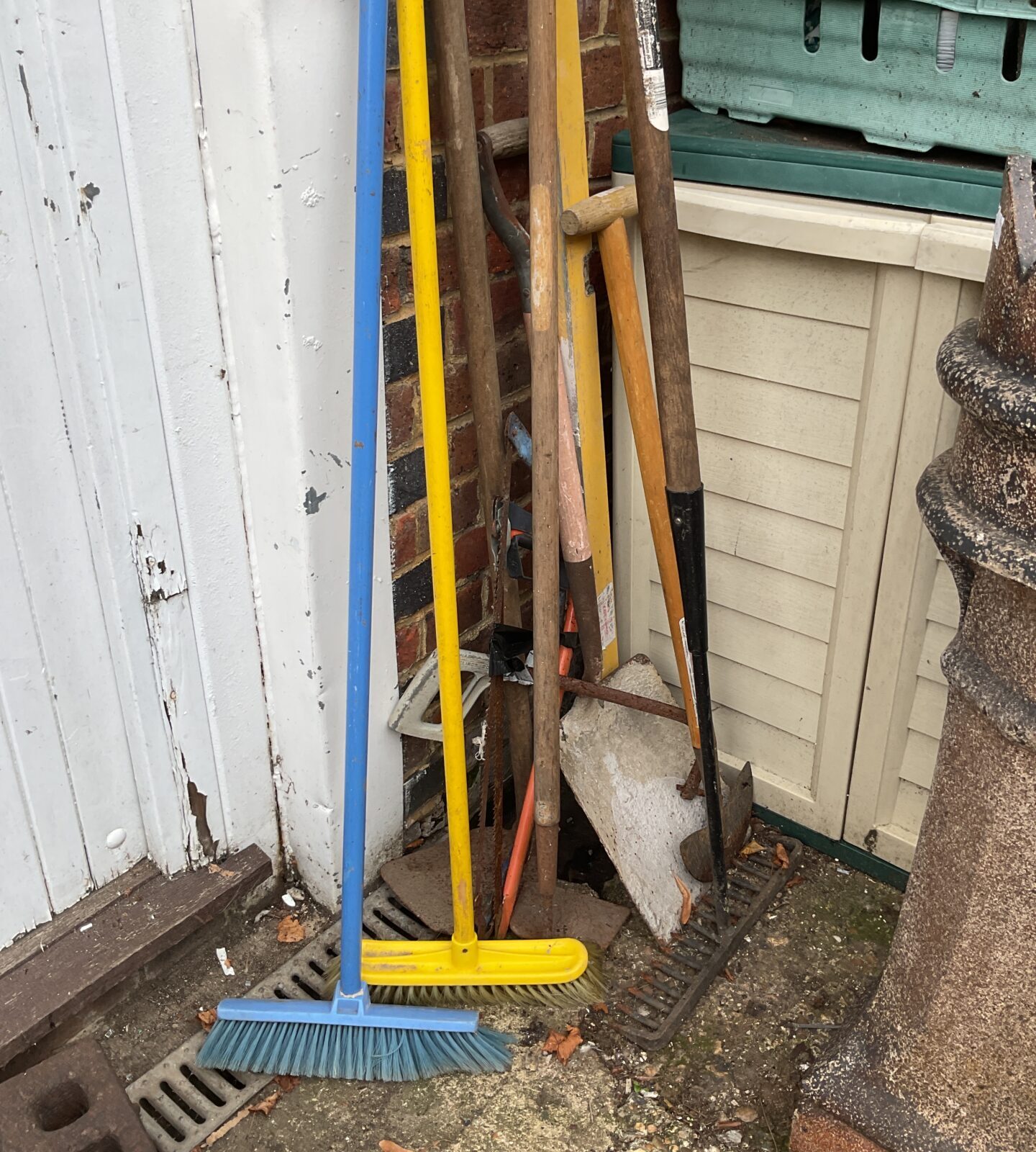 Bundle of garden tools including brooms and shovels leaning against a wall.