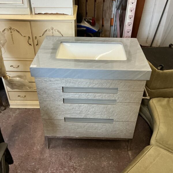 Stylish grey wash basin unit with three drawers for bathroom storage.
