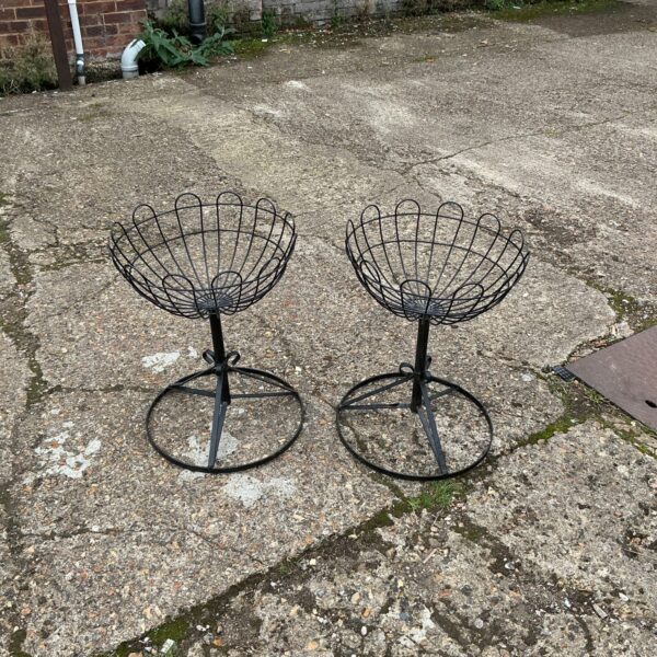 Pair of weathered metal garden basket stands in a garden.