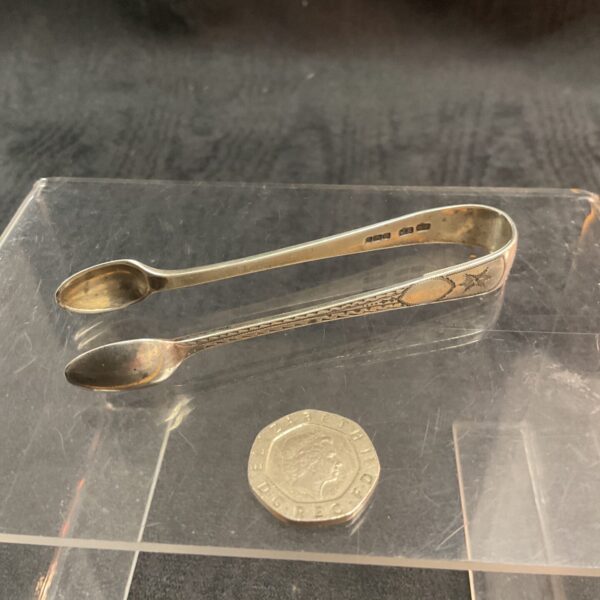 Antique silver sugar tongs with hallmarked silver detail.