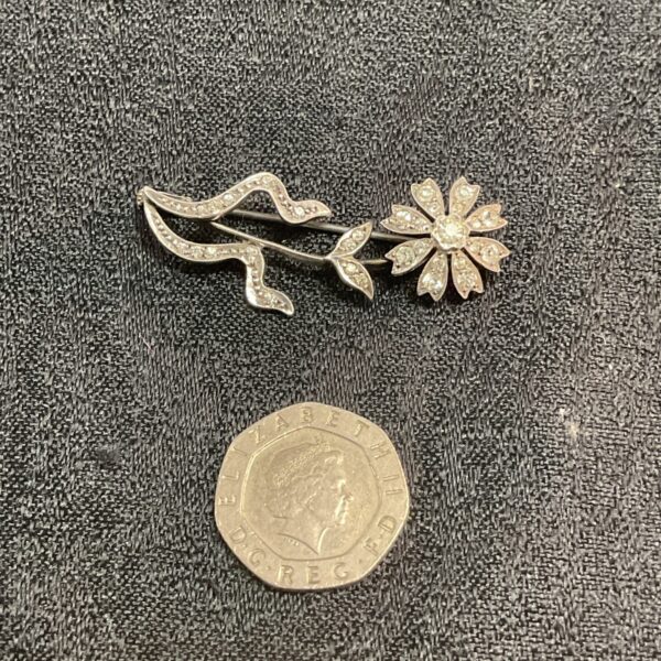 Vintage silver flower brooch with white stones on dark background.