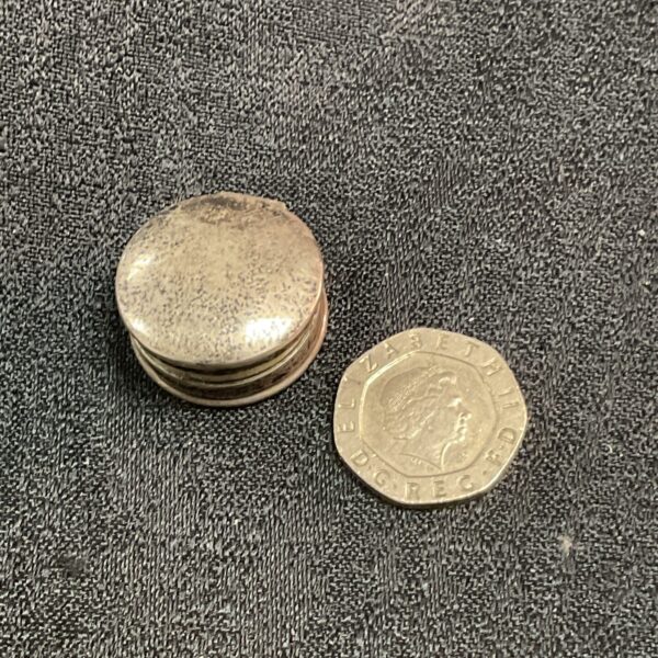 Antique silver pill pot next to a coin for scale.