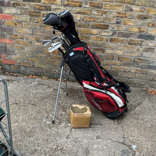 Red Wilson golf club set with bag and balls on pavement.