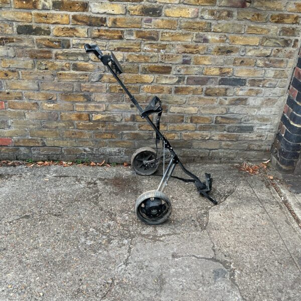 Folding golf trolley leaning against a brick wall.