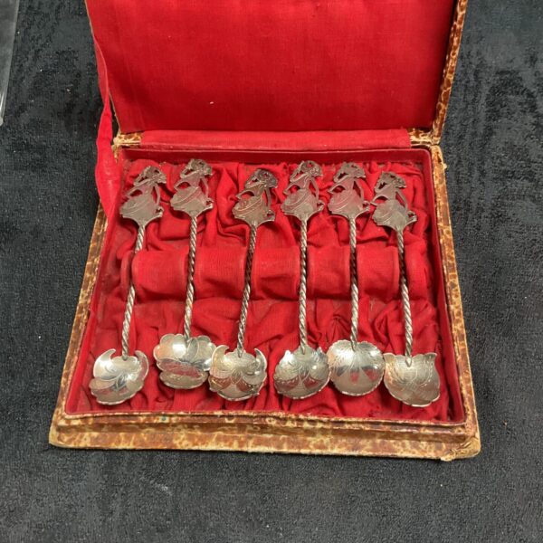 Antique Indonesian silver wyang teaspoon set displayed in a velvet-lined box.