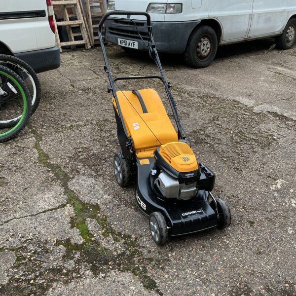 Side view of a used JCB Combi petrol lawnmower in a garden.