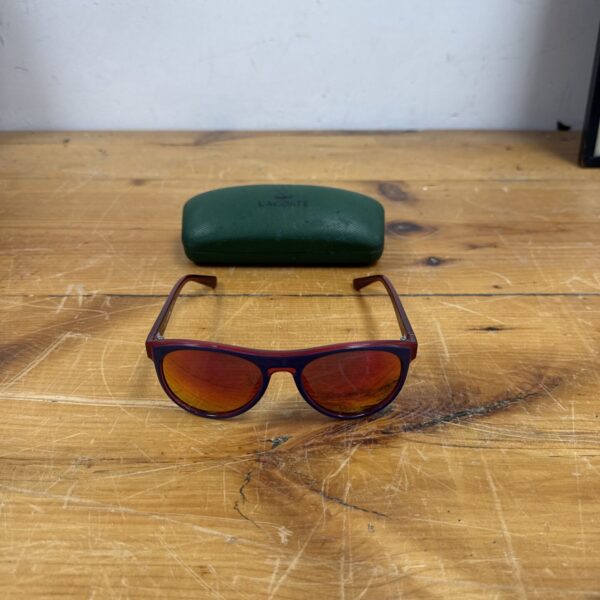 Vintage Lacoste sunglasses with mirror lenses on a wooden surface.