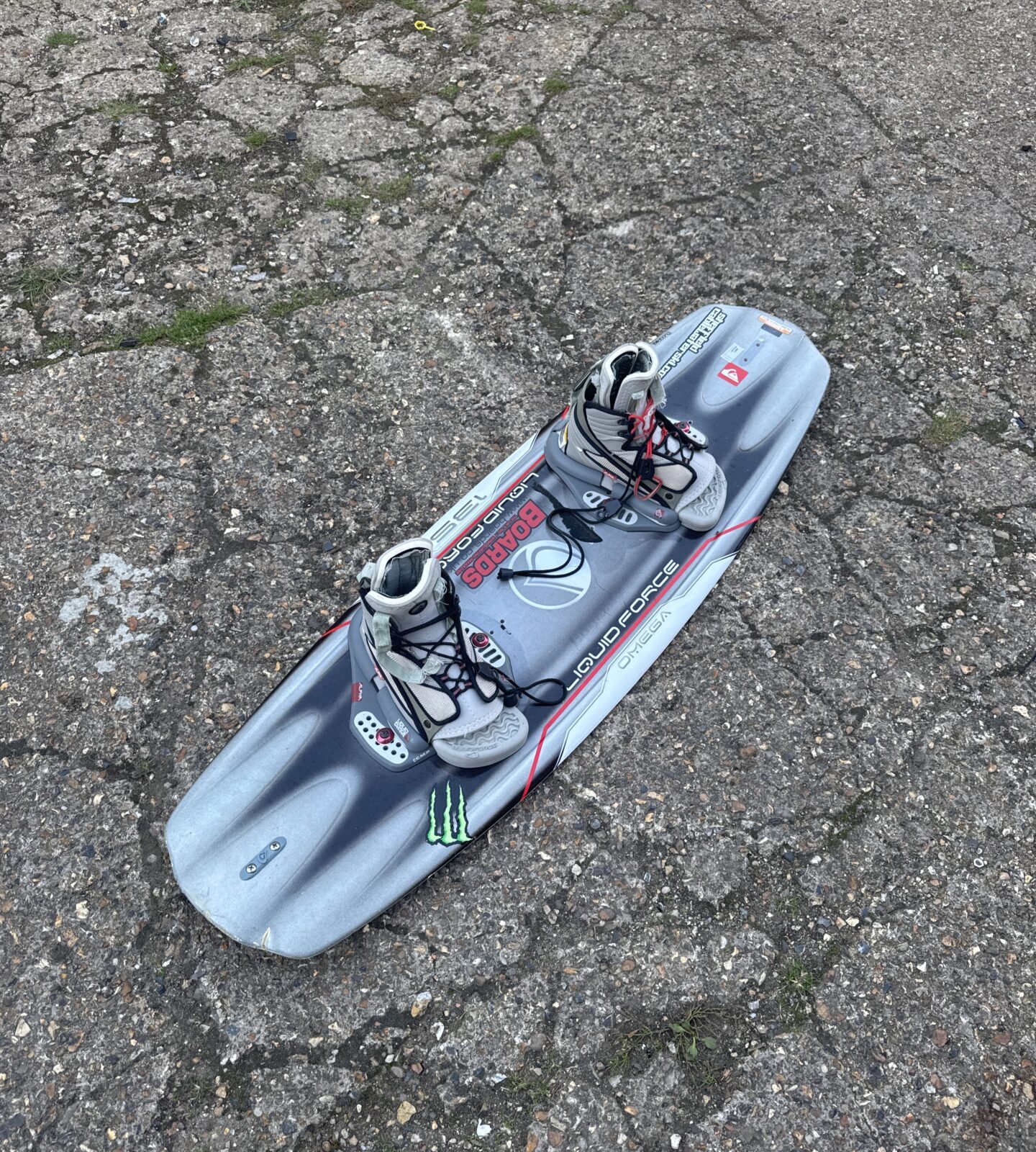 Blue Liquid Force Omega wakeboard with black bindings on asphalt.