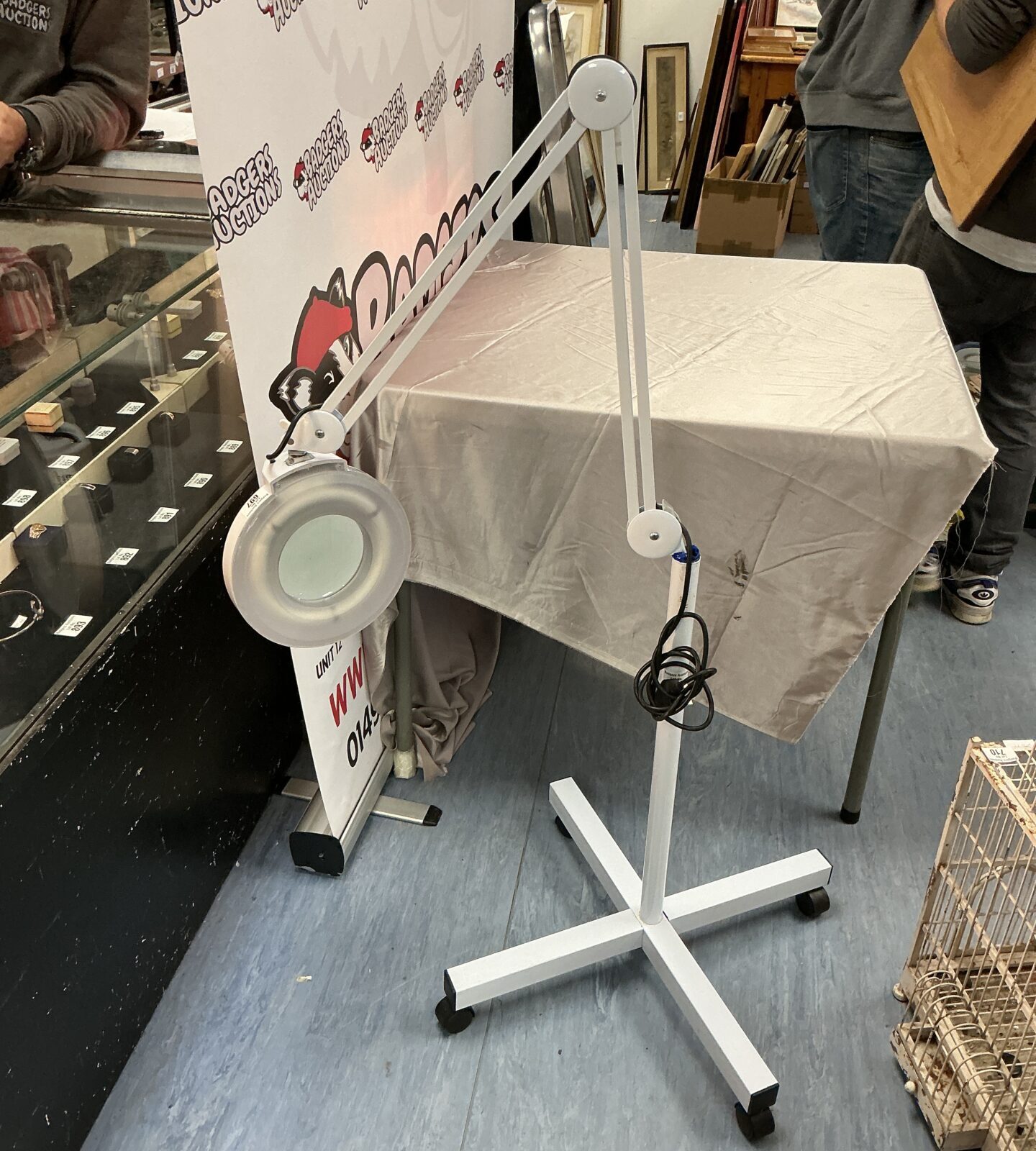 Adjustable magnifying floor lamp with large lens and caster wheels.