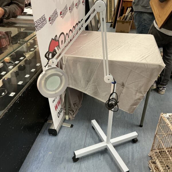 Adjustable magnifying floor lamp with large lens and caster wheels.