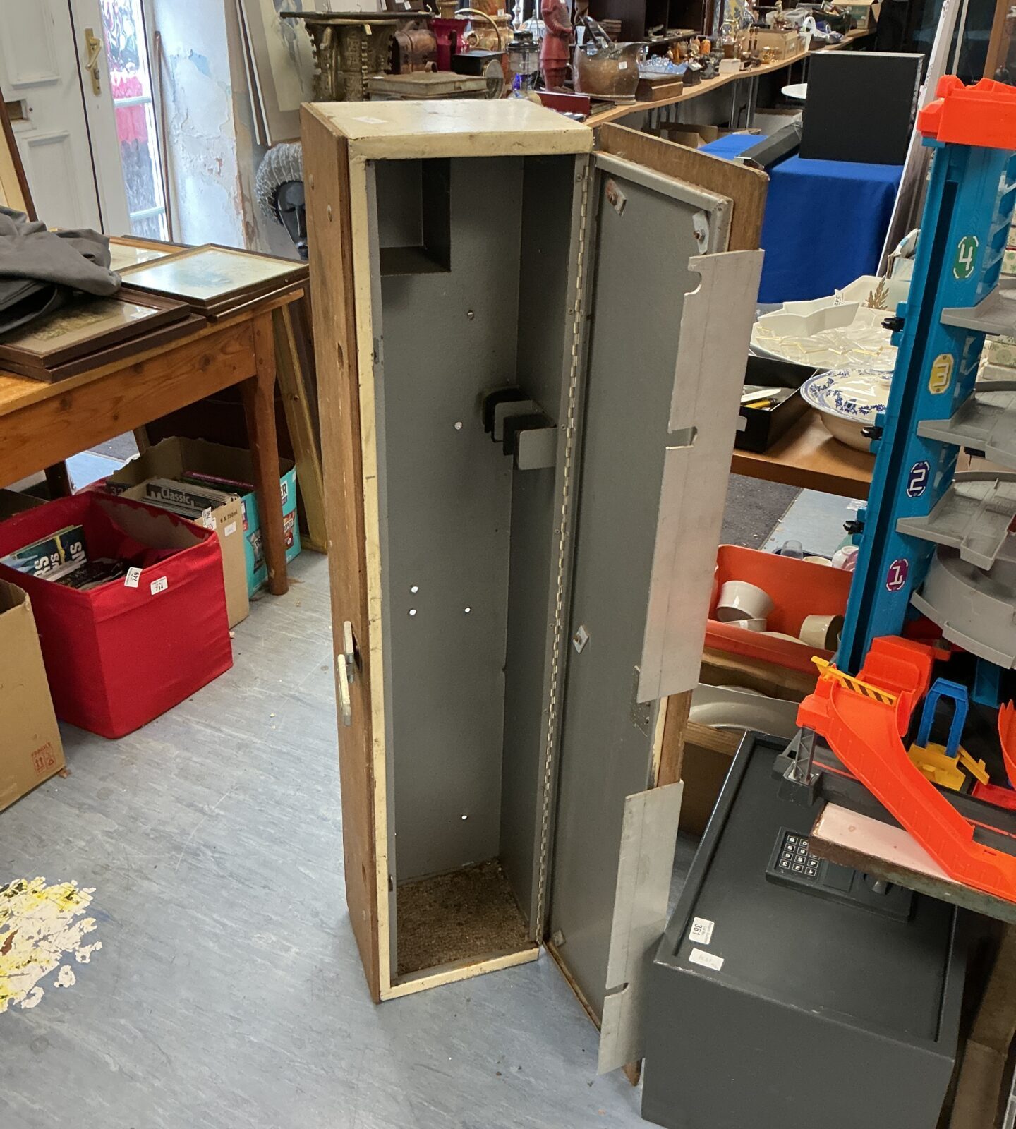 Vintage metal gun cabinet in a cluttered antique shop.