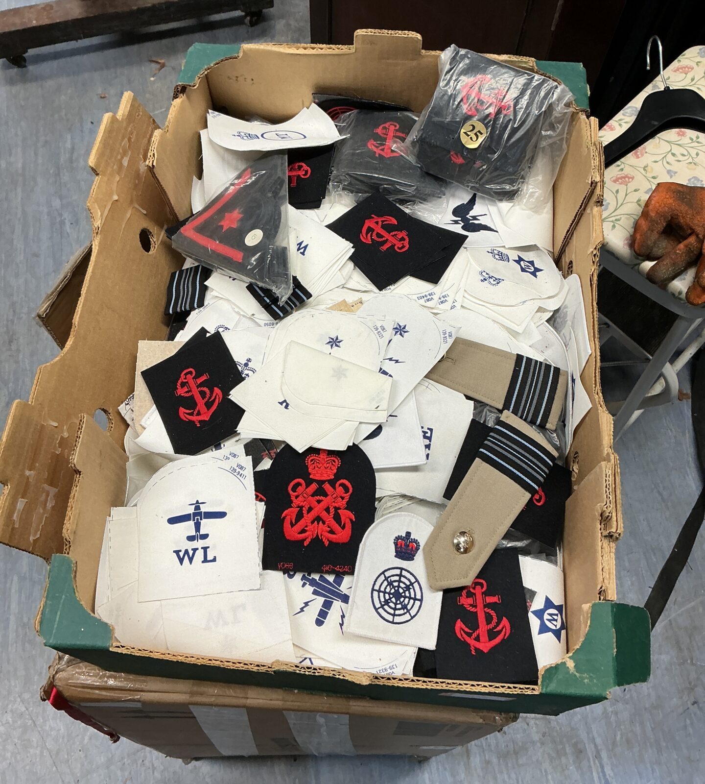 Assorted military badges in a cardboard box, collectible insignia.