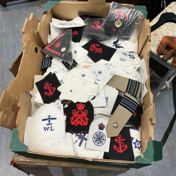 Assorted military badges in a cardboard box, collectible insignia.