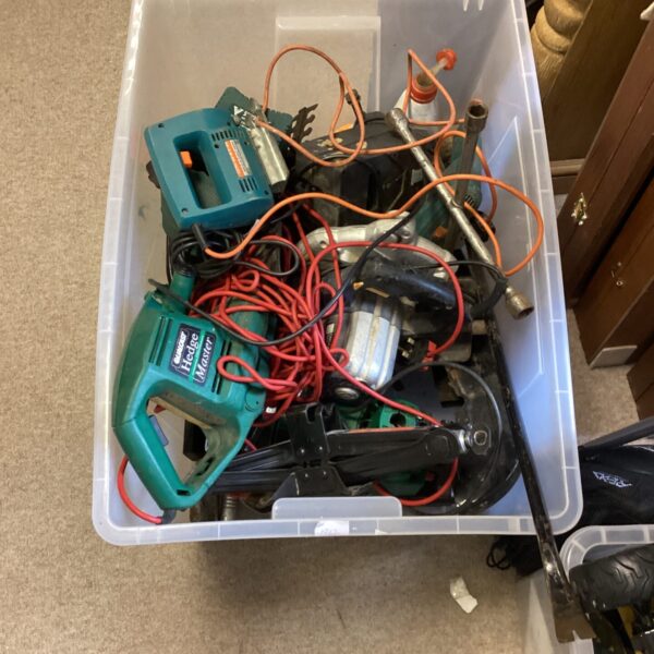 Crate filled with mixed power tools and hand tools.