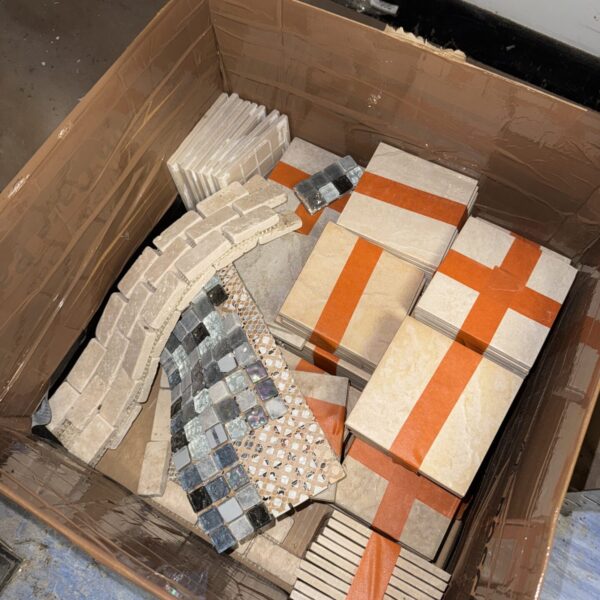 Mixed mosaic and square tile samples in a cardboard box.