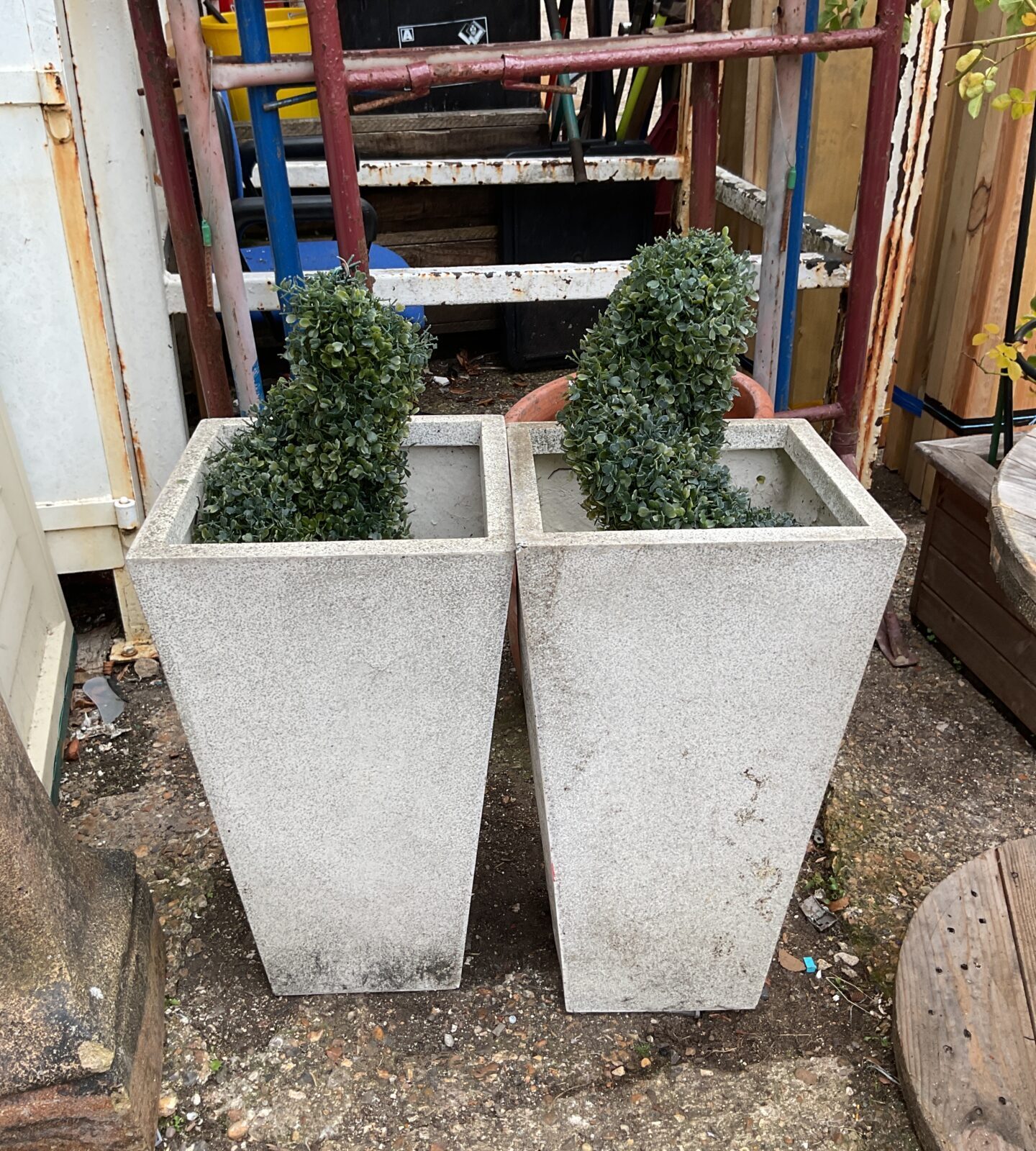 Pair of grey plastic planters with faux bushes for garden decor.