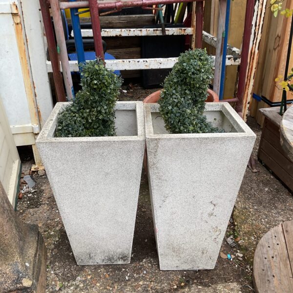 Pair of grey plastic planters with faux bushes for garden decor.