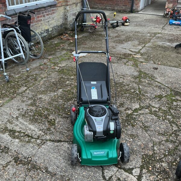 Vintage Qualcast petrol lawnmower in a garden setting.