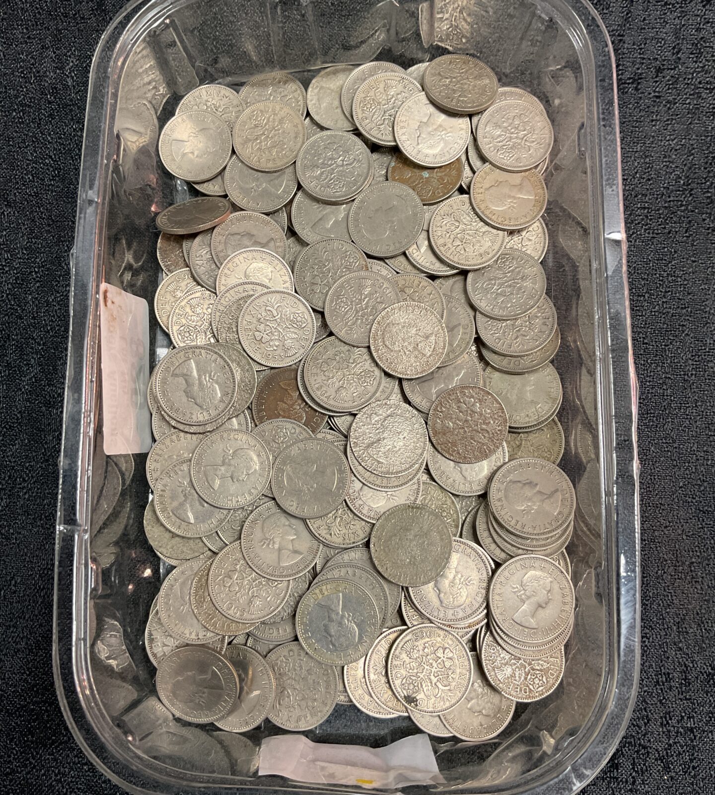 A large quantity of silver British sixpence coins in a plastic container.