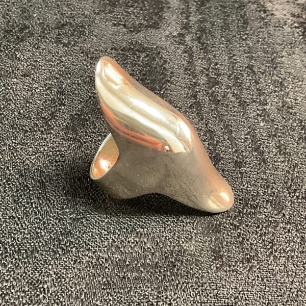 Close-up of a sleek silver knuckle ring on a textured background.