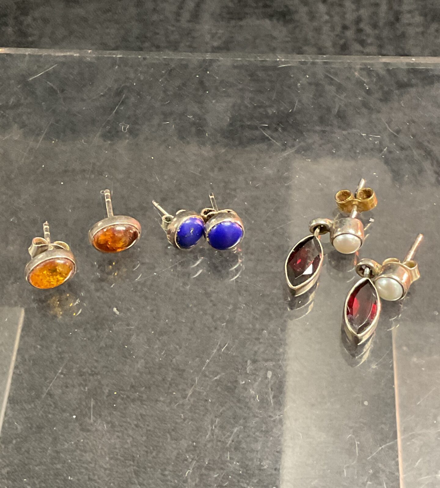 Close-up of a set of silver stud earrings with amber, blue, and pearl stones.
