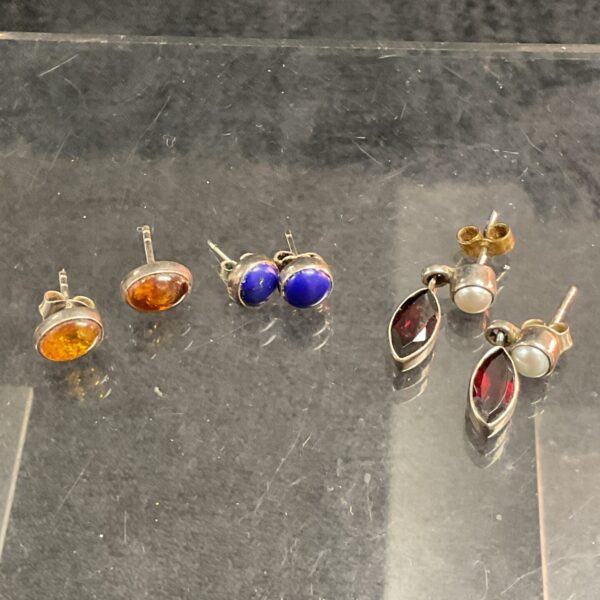 Close-up of a set of silver stud earrings with amber, blue, and pearl stones.