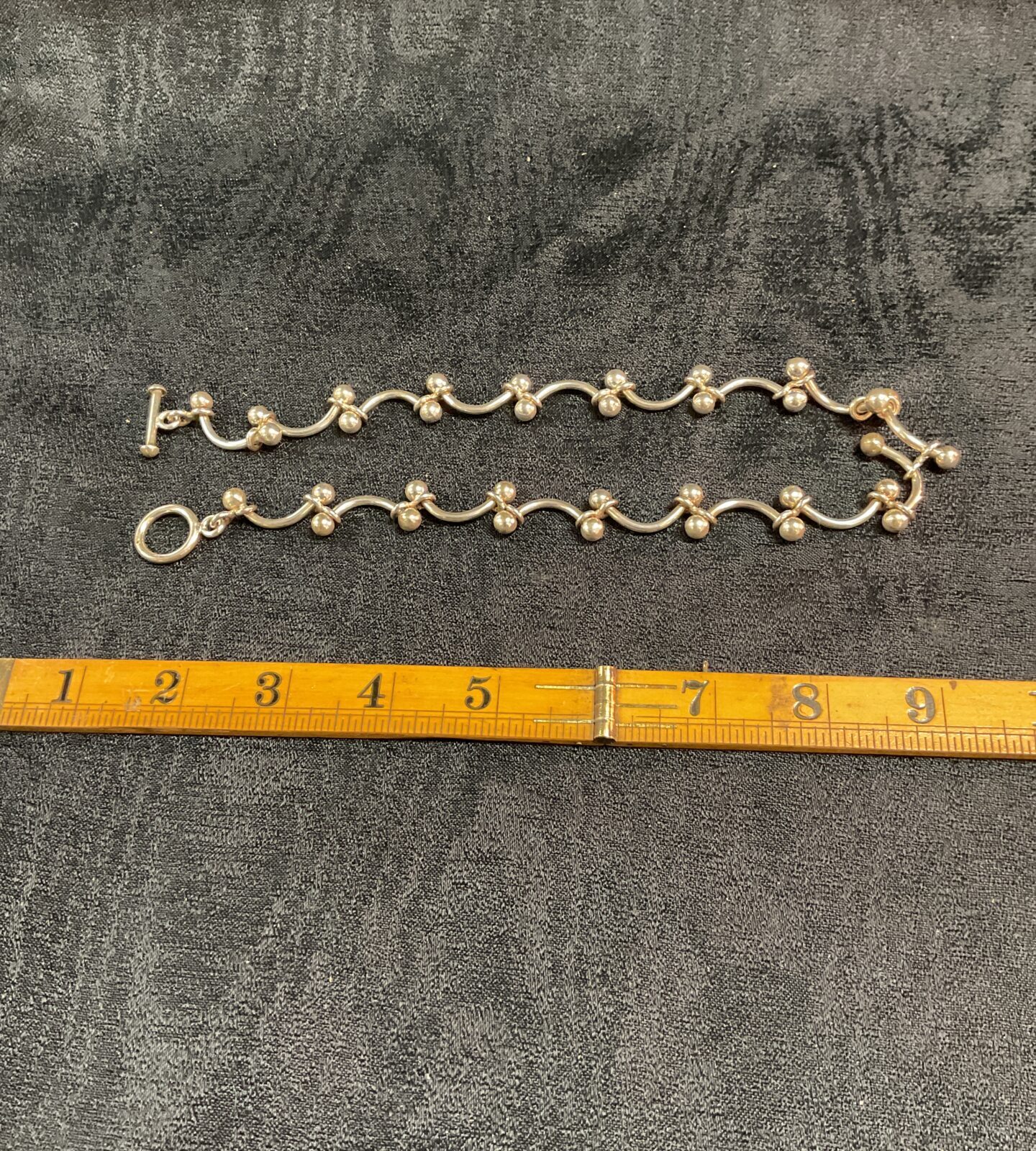 Close-up of a chunky silver T bar necklace on a neutral background.