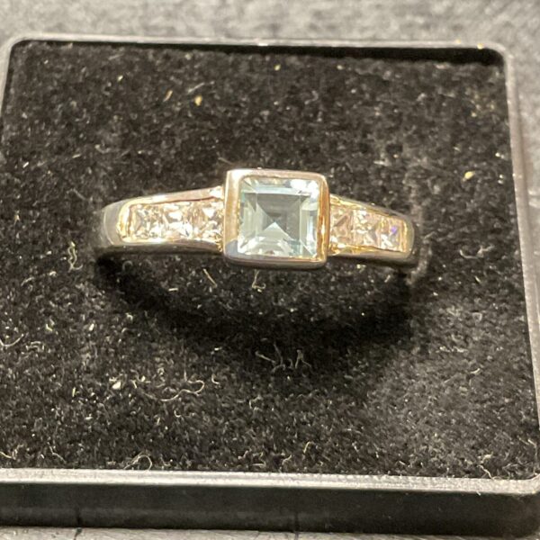 Close-up of a silver ring with a square-cut topaz gemstone.