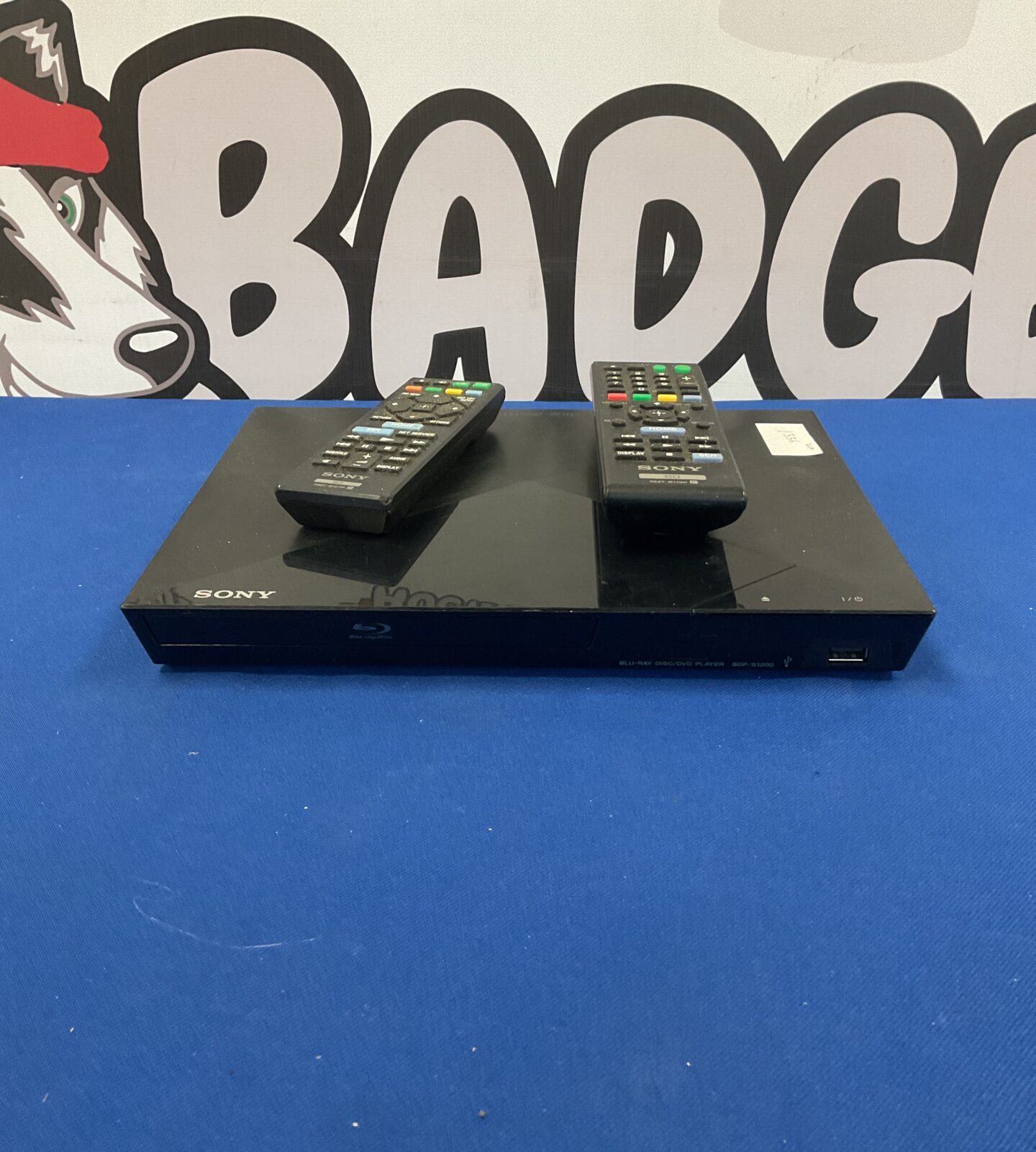 Black Sony BDP-S1200 Blu-Ray player with remote control.