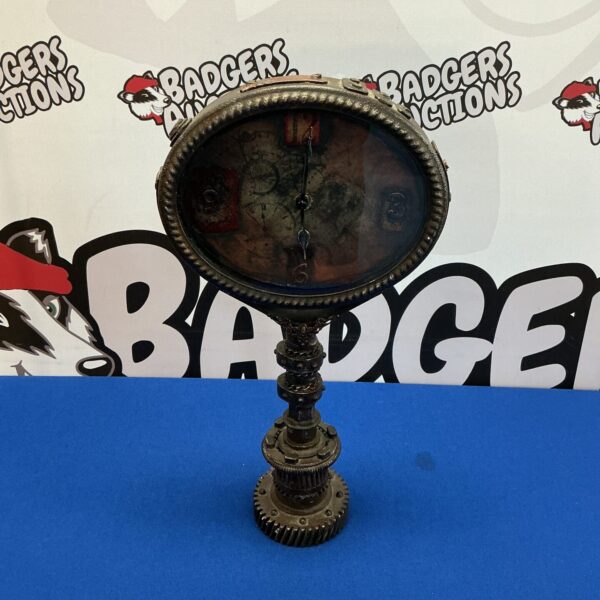 Intricate steampunk clock with a dark metal crankshaft base.
