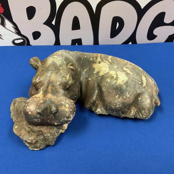 Detailed carved stone hippopotamus sculpture on blue surface.