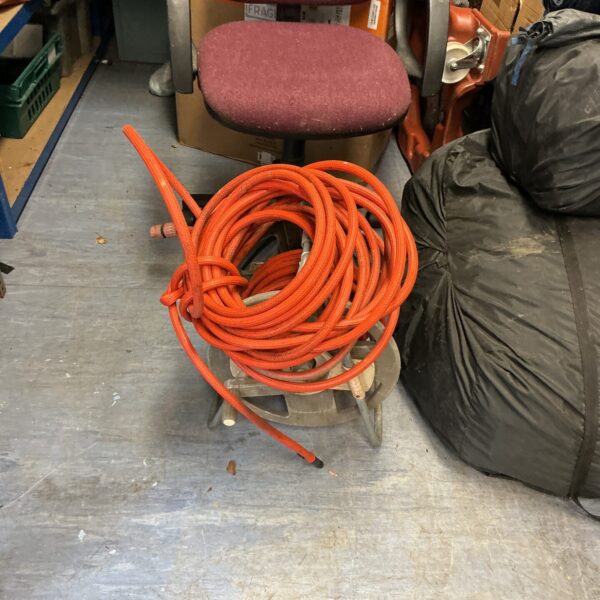 Vintage garden hose reel with red hosepipe wound around it.