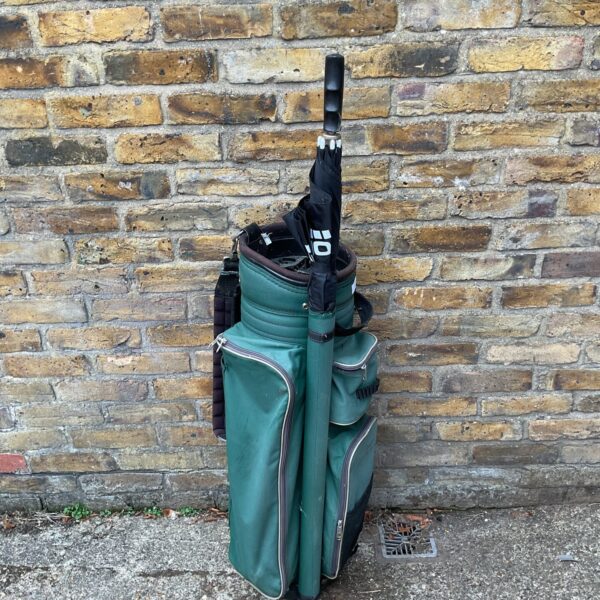 Vintage green golf bag with umbrella on brick wall.