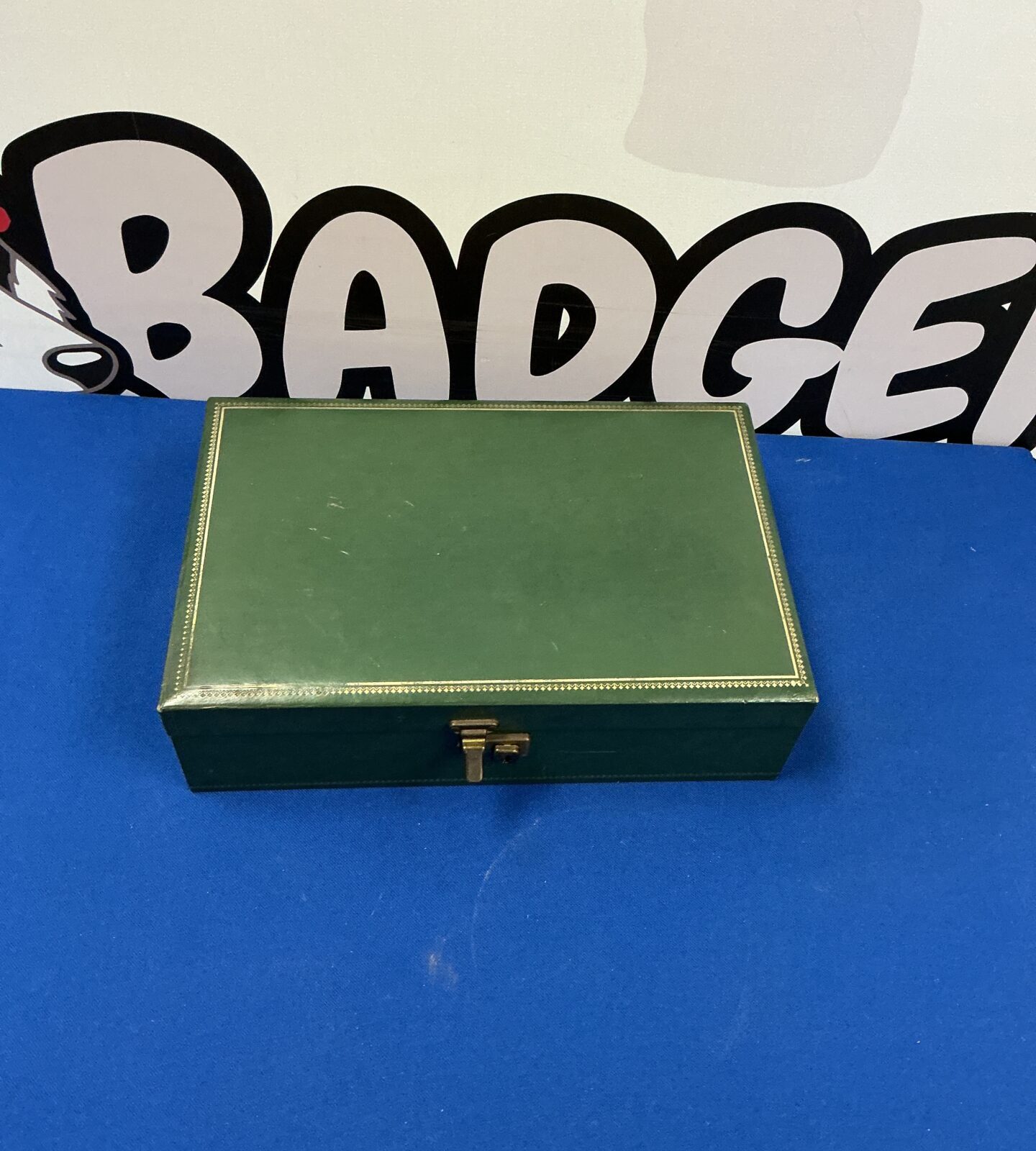 Closed vintage green leather jewellery box on a blue background.