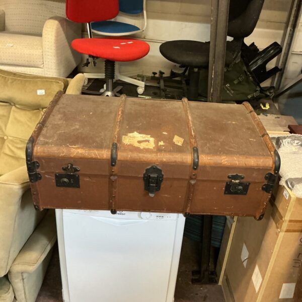 Side view of a vintage travel trunk with other furniture in the background.