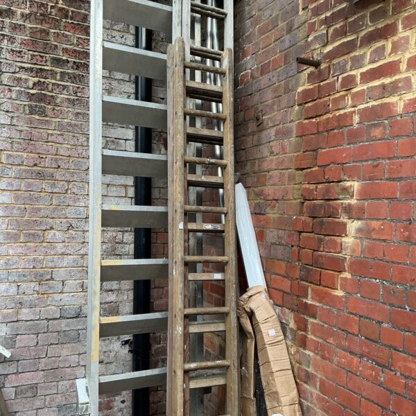 Three weathered vintage wooden ladders leaning against a brick wall.